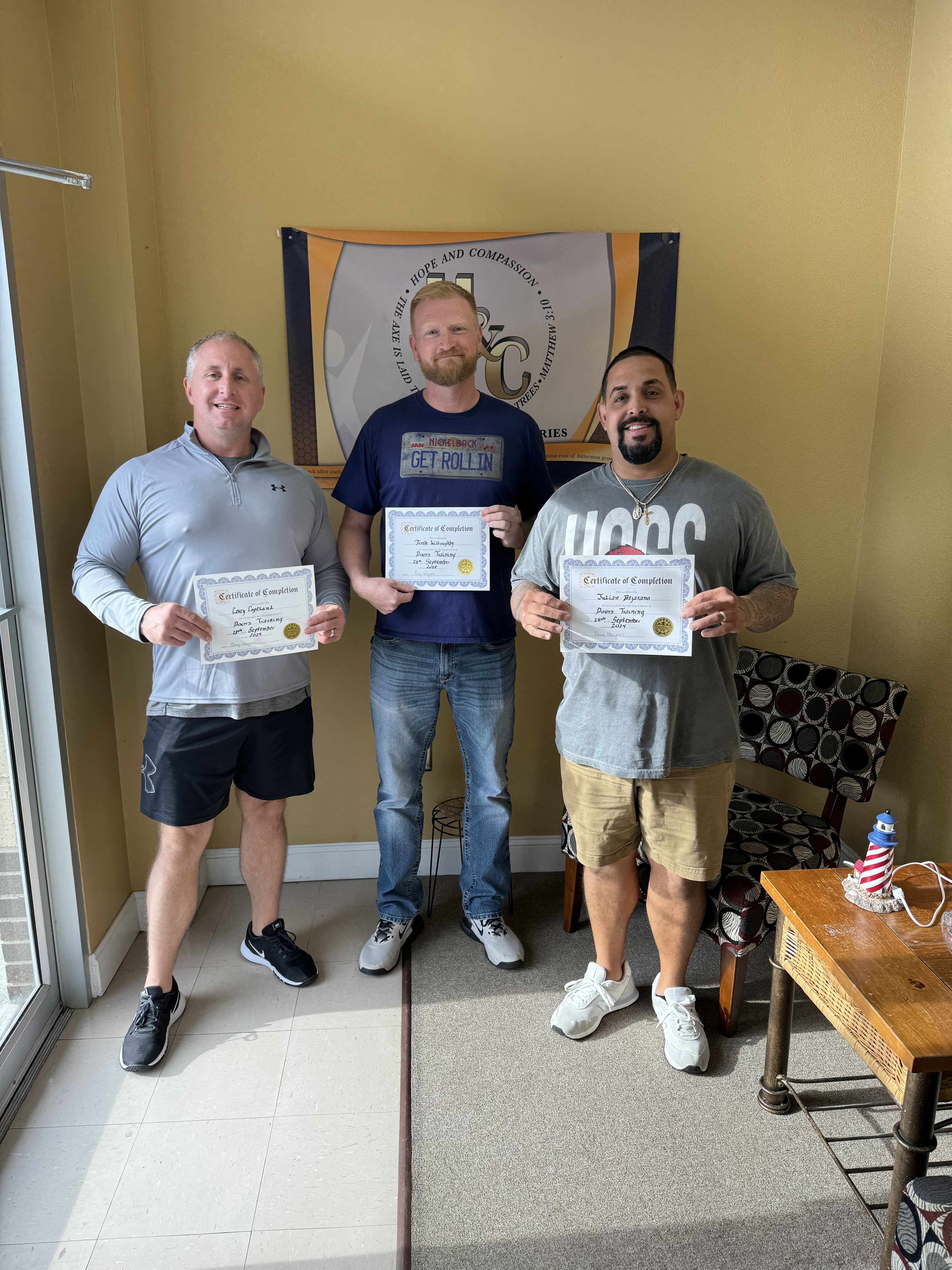 Three program graduates holding completion certificates